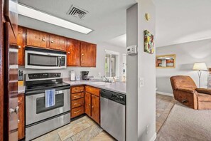 Cocina compacta con armarios de madera, microondas, estufa y lavavajillas.