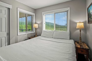 Un dormitorio con una cama grande, dos mesitas de noche con lámparas y dos ventanas con persianas.