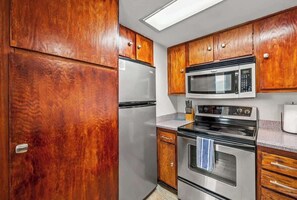 Eine Küche mit Holzausstattung, einem Edelstahlkühlschrank, einer Mikrowelle und einem Backofen.