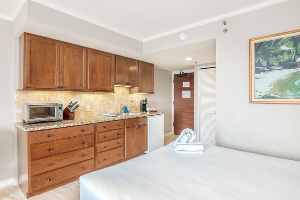 A compact kitchen with wooden cabinets, a microwave, and a small refrigerator.