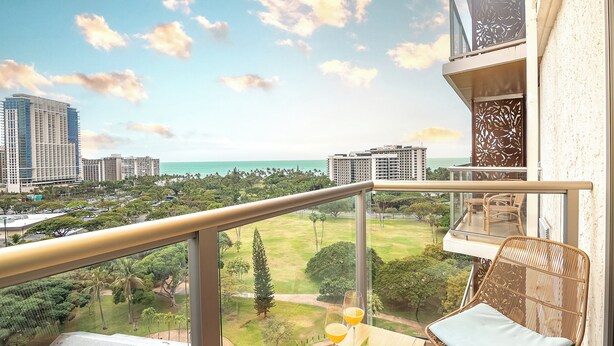 Un balcon offrant une vue sur le paysage urbain, une zone herbeuse et une étendue d’eau.