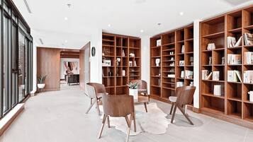 Una biblioteca moderna con estanterías de madera, sillones de cuero y una alfombra blanca.