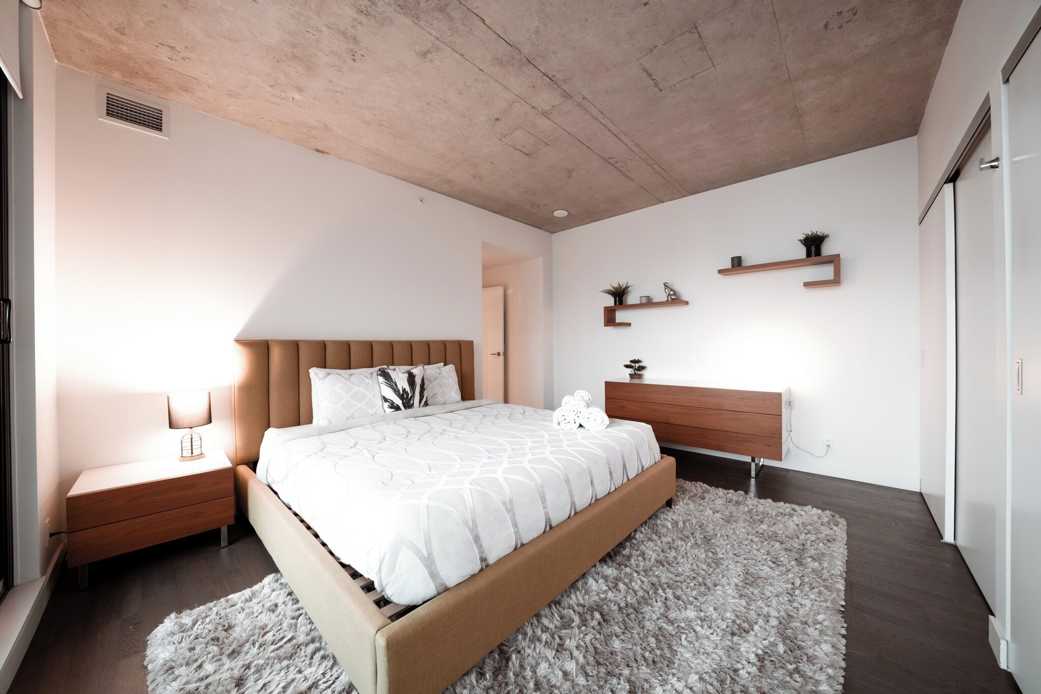 A modern bedroom with a large bed, wooden nightstands, a fluffy rug, and built-in shelves.