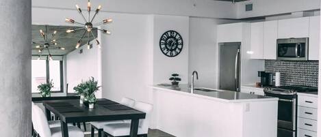 Una cocina moderna con armarios blancos, un refrigerador de acero inoxidable y un microondas empotrado.