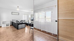 A modern living room with a sofa, a coffee table, and a TV. There is a white cabinet and a small table with a chair.