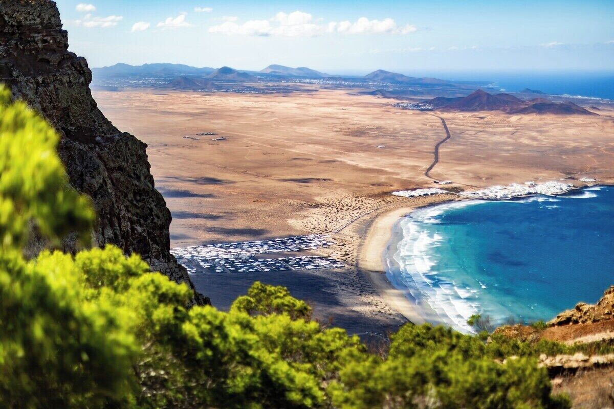 A coastal landscape with a rocky cliff, a beach, and distant mountains.
