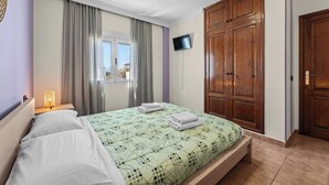 A hotel room with a bed, a TV mounted on the wall, and a wooden wardrobe.
