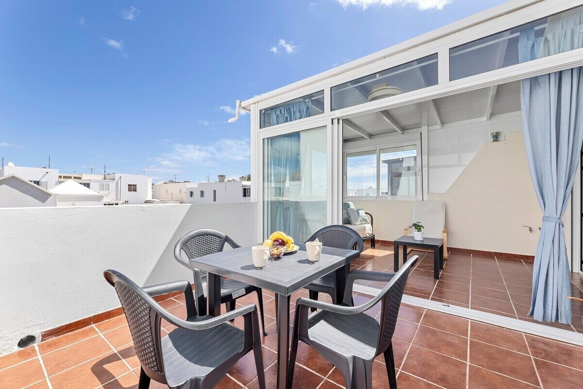 A rooftop terrace with a table and chairs, a view of the cityscape, and a building with large windows and a curtain.