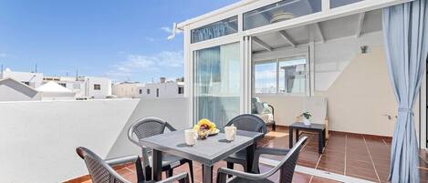 A rooftop terrace with a table and chairs, a view of the cityscape, and a building with large windows and a curtain.