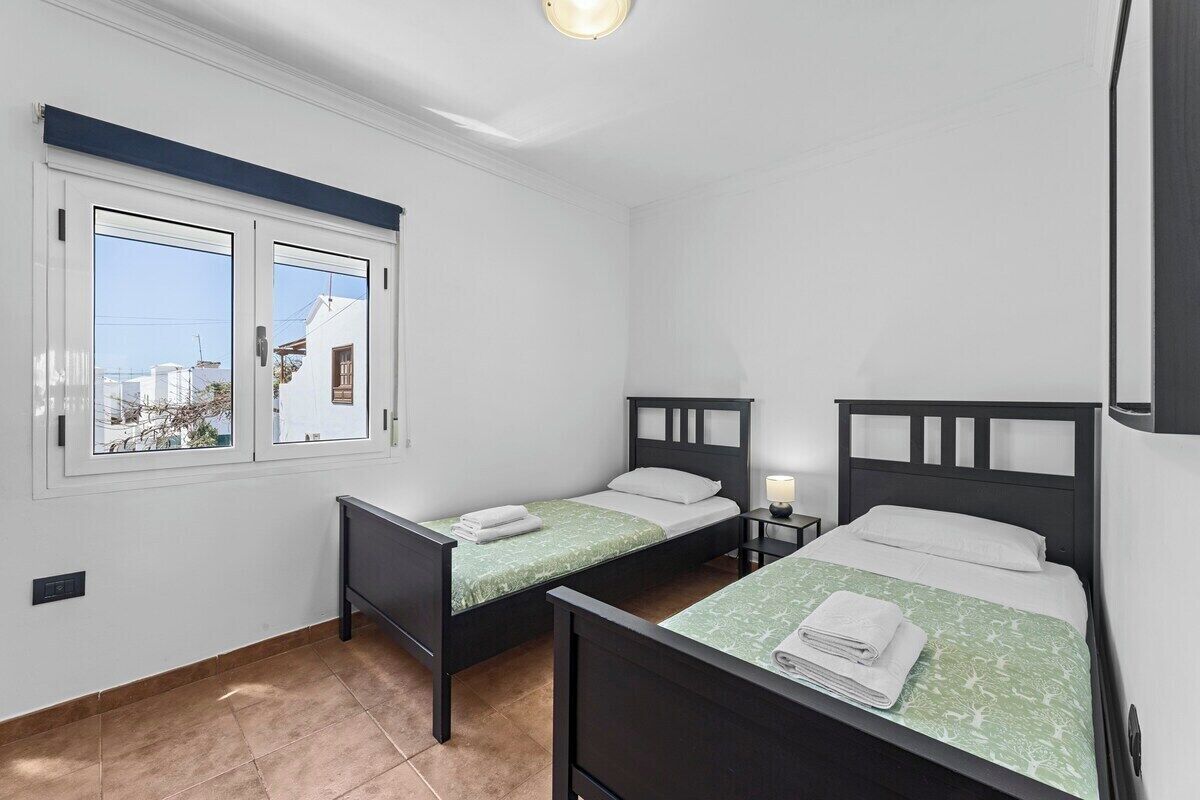 Une chambre avec deux lits simples, une fenêtre donnant sur des immeubles et un luminaire au plafond.
