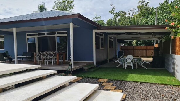 Uma área de varanda coberta com mobiliário externo, um pequeno deck e um gramado bem cuidado.