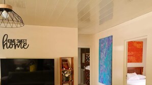 Sala de estar con televisor, mueble de madera para entretenimiento y sofá con cojines estampados.