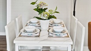 Ein Essbereich mit einem weißen Tisch, gedeckt für vier Personen, einer Blumenvase und zwei hohen Stehlampen.