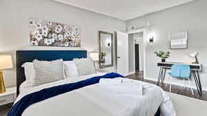 Ein Hotelzimmer mit einem großen Bett, einem Schreibtisch mit Stuhl, einem Spiegel und einem Wandbild.
