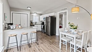 Eine moderne Küche mit weißen Schränken, einem Edelstahlkühlschrank und einem Essbereich mit weißem Tisch und Stühlen.