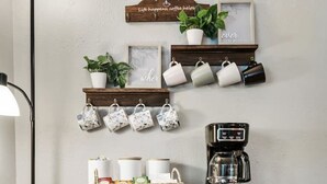 A kitchen area with a wooden countertop, a coffee maker, and a shelf with mugs and a sign. - Vivid 1BD: TCU Walkable, Inspiring & Restful! (Fort Worth)