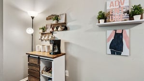 A kitchen area with a coffee machine, mugs, and a shelf with plants. - Vivid 1BD: TCU Walkable, Inspiring & Restful! (Fort Worth)