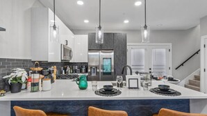 Une cuisine moderne dotée d’un îlot central, d’appareils électroménagers en acier inoxydable et de luminaires suspendus.