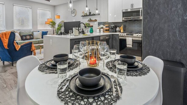 Une cuisine moderne avec des meubles blancs, un îlot central et un coin repas agrémenté de vaisselle et de verrerie noires.