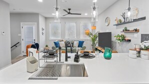 Une cuisine moderne dotée d’un îlot central, d’un évier en acier inoxydable et de luminaires suspendus.