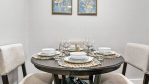 Comedor con una mesa redonda dispuesta para cuatro personas, con detalles en madera oscura, sillas tapizadas en tonos claros y un mantel blanco sencillo.