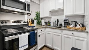 Una cocina moderna con armarios blancos, estufa de acero inoxidable, microondas y cafetera.