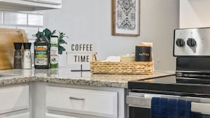 Cozinha com armários brancos, um letreiro de café, fogão e diversos utensílios de cozinha.