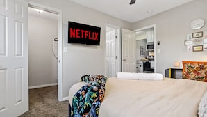 Um quarto com uma cama, uma televisão fixada na parede e uma porta que dá para o banheiro.