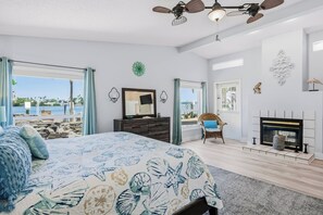 A bedroom with a bed, a dresser, a chair, a fireplace, and a view of the ocean.