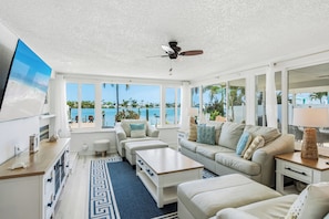A spacious living room with a large window overlooking a scenic ocean view, a ceiling fan, and a modern interior design.