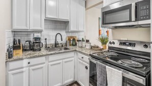A modern kitchen with white cabinets, a stainless steel microwave, a stove, and various appliances. - Where It's All Happening: 1BD in the Mid of Action (Arlington)