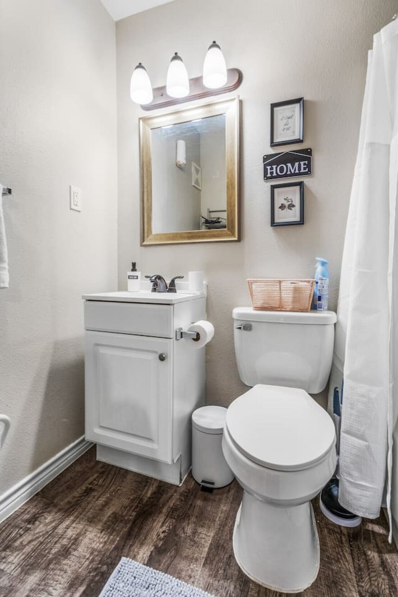 Une salle de bain avec des toilettes blanches, un lavabo avec un miroir au-dessus, et un rideau de douche.