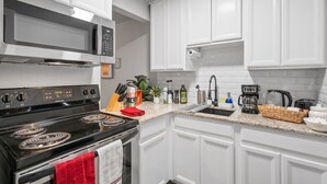 A modern kitchen with white cabinets, a black stove, a microwave, and various kitchen appliances and utensils. - Steps Away from the Heart of the FUN!AT&T Walkable (Arlington)