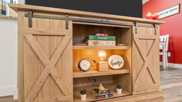 A wooden storage unit with a sliding door, containing poker boxes, a clock, a decorative item, and small plants. - Steps Away from the Heart of the FUN!AT&T Walkable (Arlington)