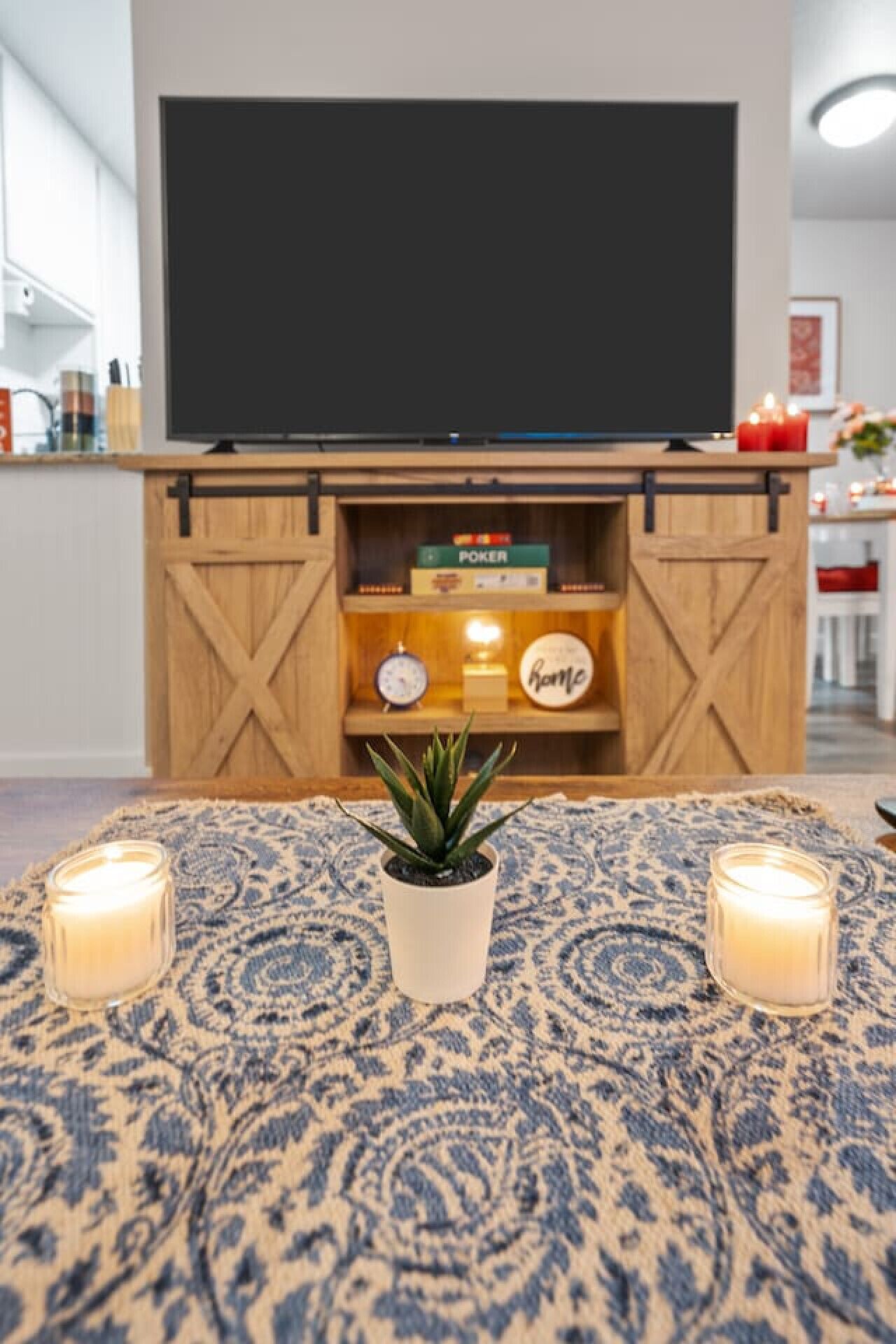 Un salon avec un téléviseur fixé au mur, un mur en bois, une petite étagère avec des jetons de poker, une horloge et un chandelier.