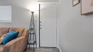 A room with a beige sofa, a white door, a floor lamp, and a framed picture on the wall. - Steps Away from the Heart of the FUN!AT&T Walkable (Arlington)
