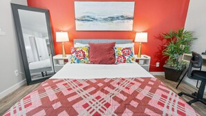 A hotel room with a bed, two bedside lamps, a large mirror, a red wall, a painting, a potted plant, and a chair. - Steps Away from the Heart of the FUN!AT&T Walkable (Arlington)