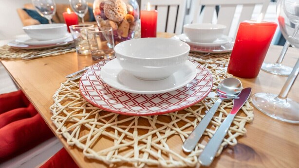 A dining table set with white plates, red patterned napkins, and silverware.