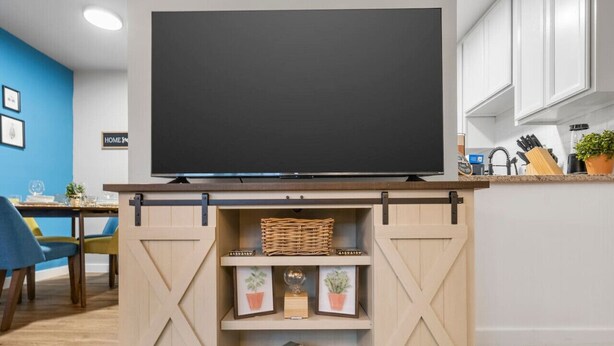 A modern living room with a mounted flat-screen TV, a wooden entertainment unit with shelves, and a dining area with a blue chair and table. - Sapphire 1BD: AT&T Walkable, Calming & Joyful ! (Arlington)