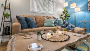 A cozy living room with a wooden coffee table, a sofa with cushions, a ladder with plants, and a blue wall. - Sapphire 1BD: AT&T Walkable, Calming & Joyful ! (Arlington)
