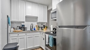 A modern kitchen with white cabinets, stainless steel appliances, and a trash bin. - Sapphire 1BD: AT&T Walkable, Calming & Joyful ! (Arlington)