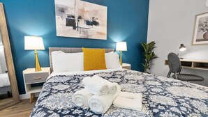 A hotel room with a large bed, two bedside lamps, a desk with a chair, and a potted plant. - Blissful 1BD:AT&T Walkable, Modern & Ground-Level! (Arlington)