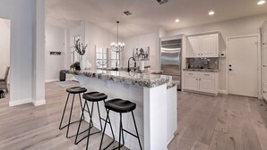 A modern kitchen with a central island, bar stools, white cabinetry, and stainless steel appliances.