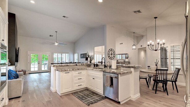 A spacious kitchen with white cabinetry, a central island, and a dining area with black chairs.