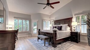 A bedroom with a large bed, a ceiling fan, a wooden nightstand, and a window with shutters.