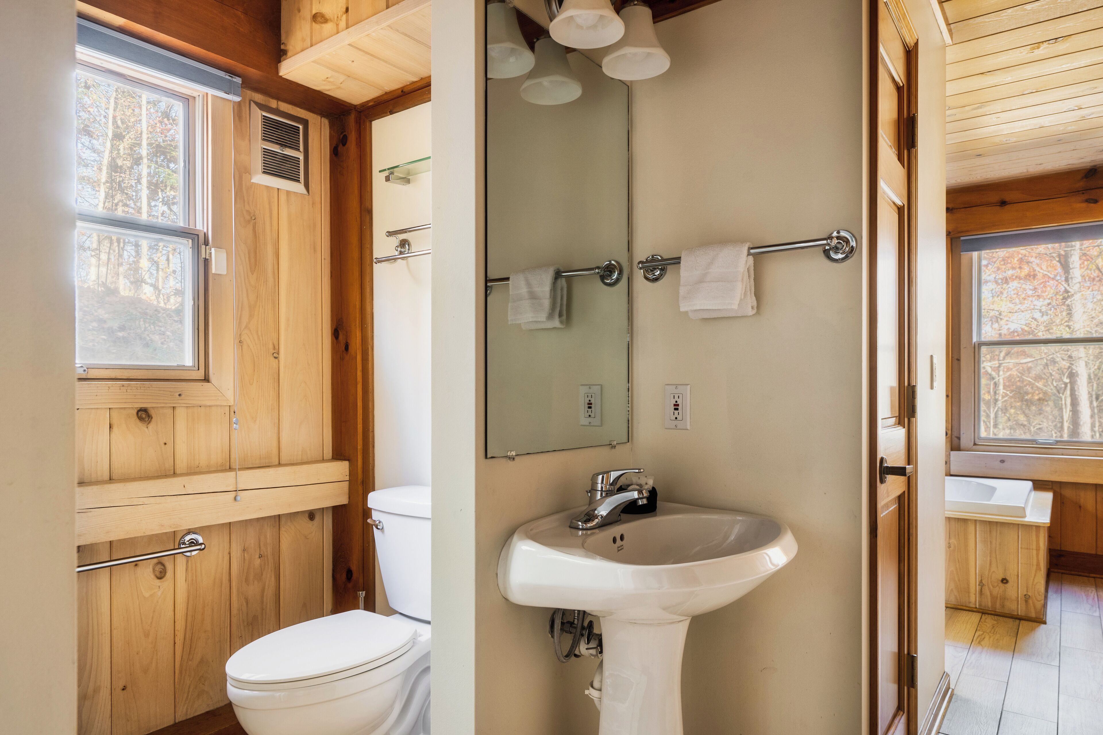 A wooden cabin bathroom with a toilet, sink, and mirror.