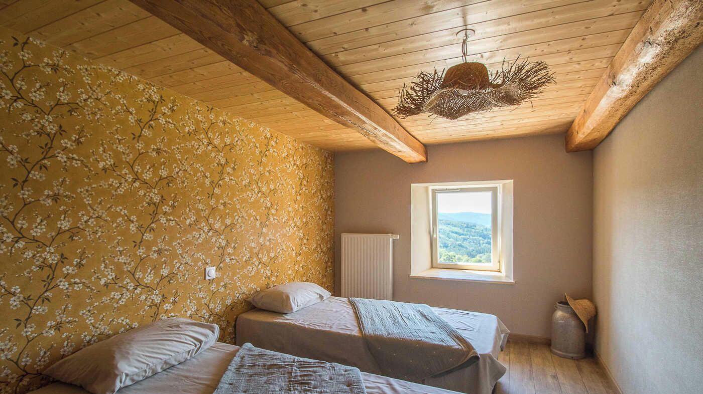 A bedroom with two beds, a window with a view, wooden beams on the ceiling, and a radiator.