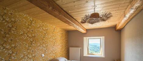 A bedroom with two beds, a window with a view, wooden beams on the ceiling, and a radiator.