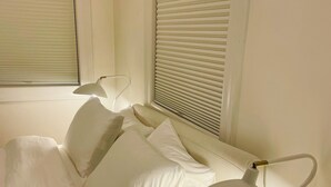 Ein ordentlich bezogenes Bett mit weißer Bettwäsche und Kissen, eine moderne Stehlampe und ein мраморный Nachttisch.