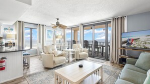 A spacious living area with a large window, a ceiling fan, and a television. - GULF-FRONT CONDO, POOLS, SPLASH PAD, LOTS OF AMENITIES! (Orange Beach)